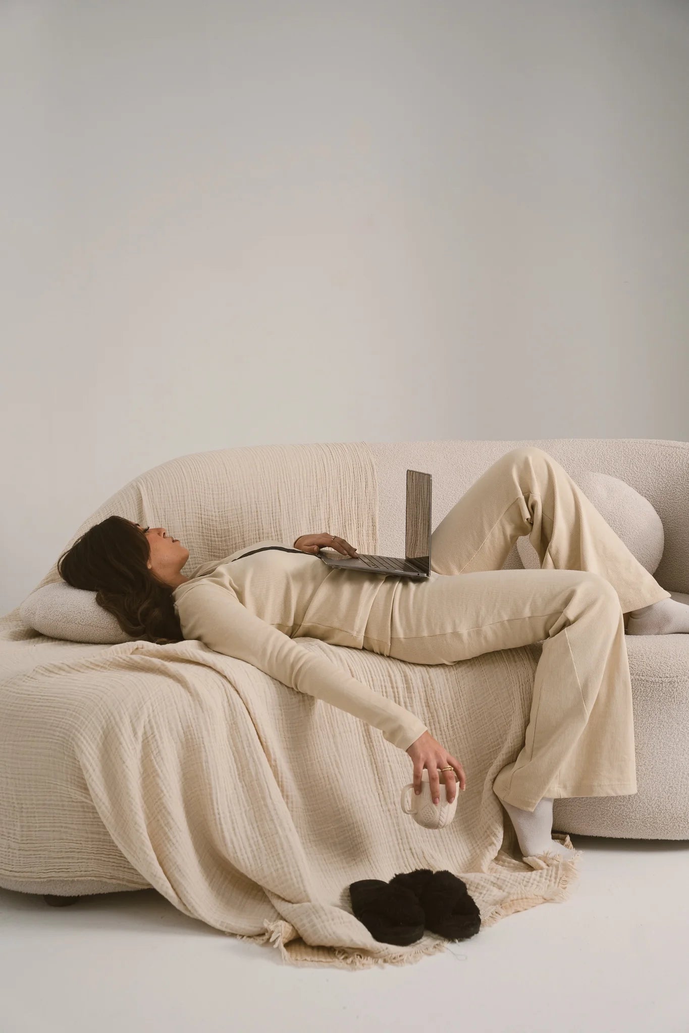 Person lying on a couch with a blanket and laptop in a minimalistic room
