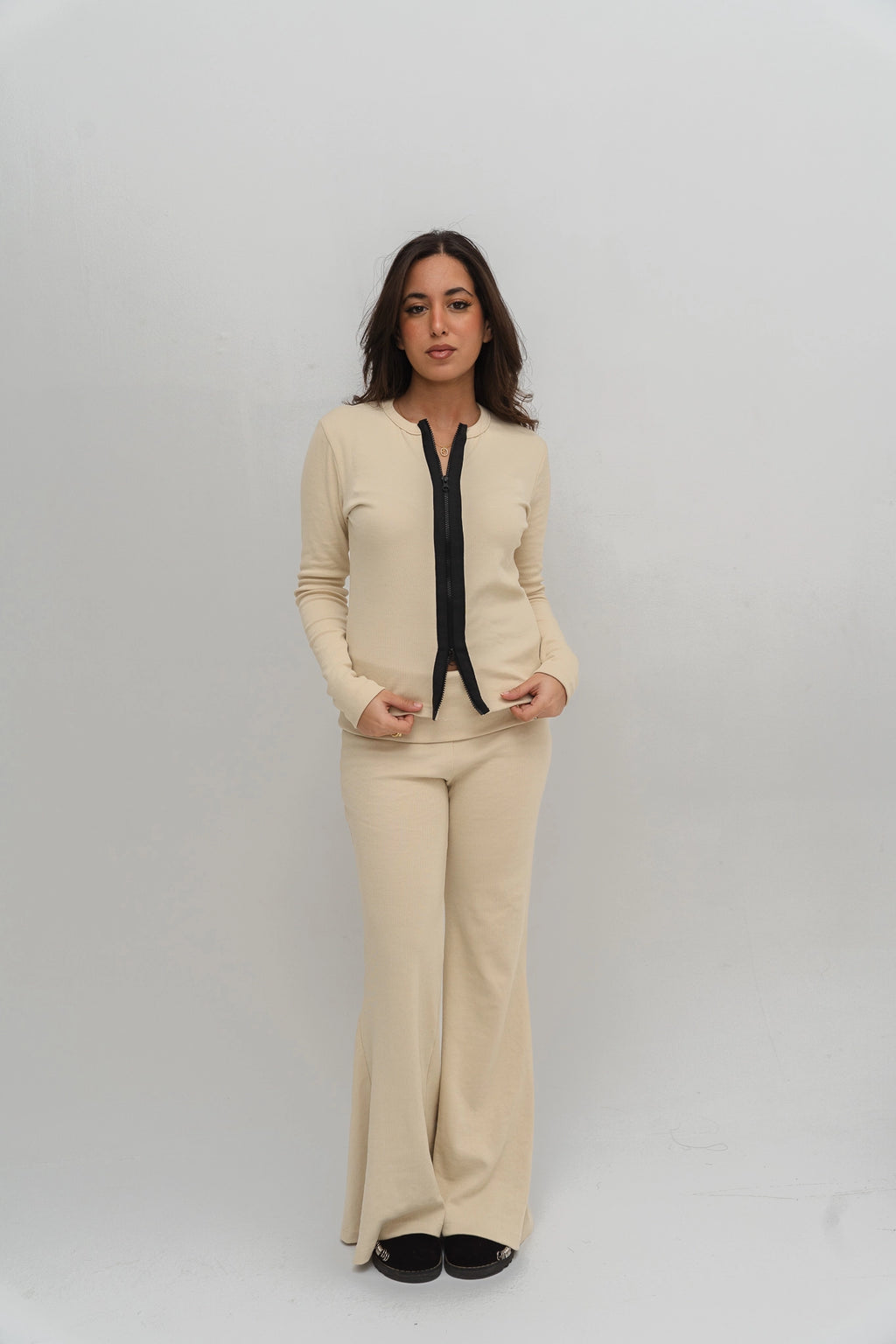 Woman wearing a beige outfit with a black top against a white background