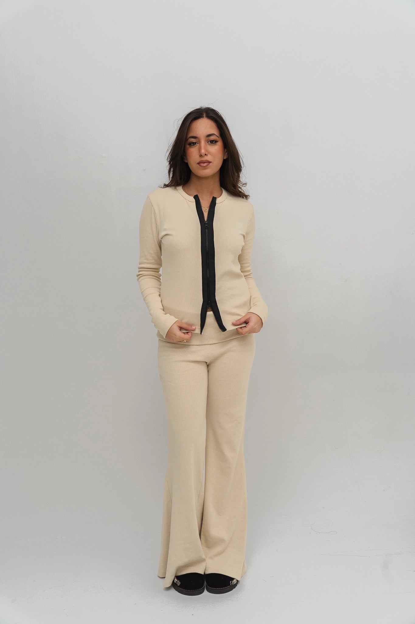 Woman wearing a beige outfit with a black top against a white background