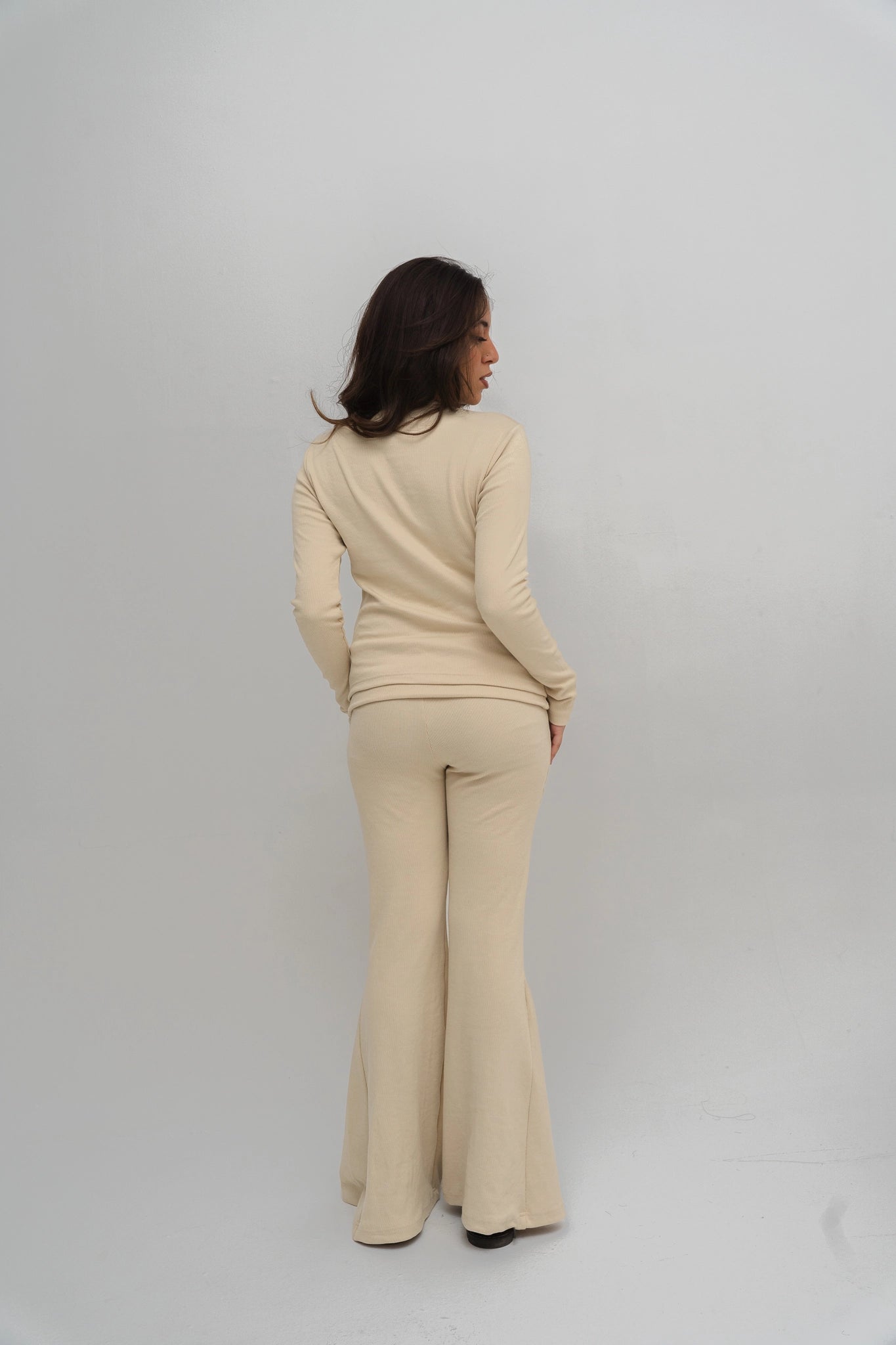 Woman wearing a beige outfit with flared pants on a white background
