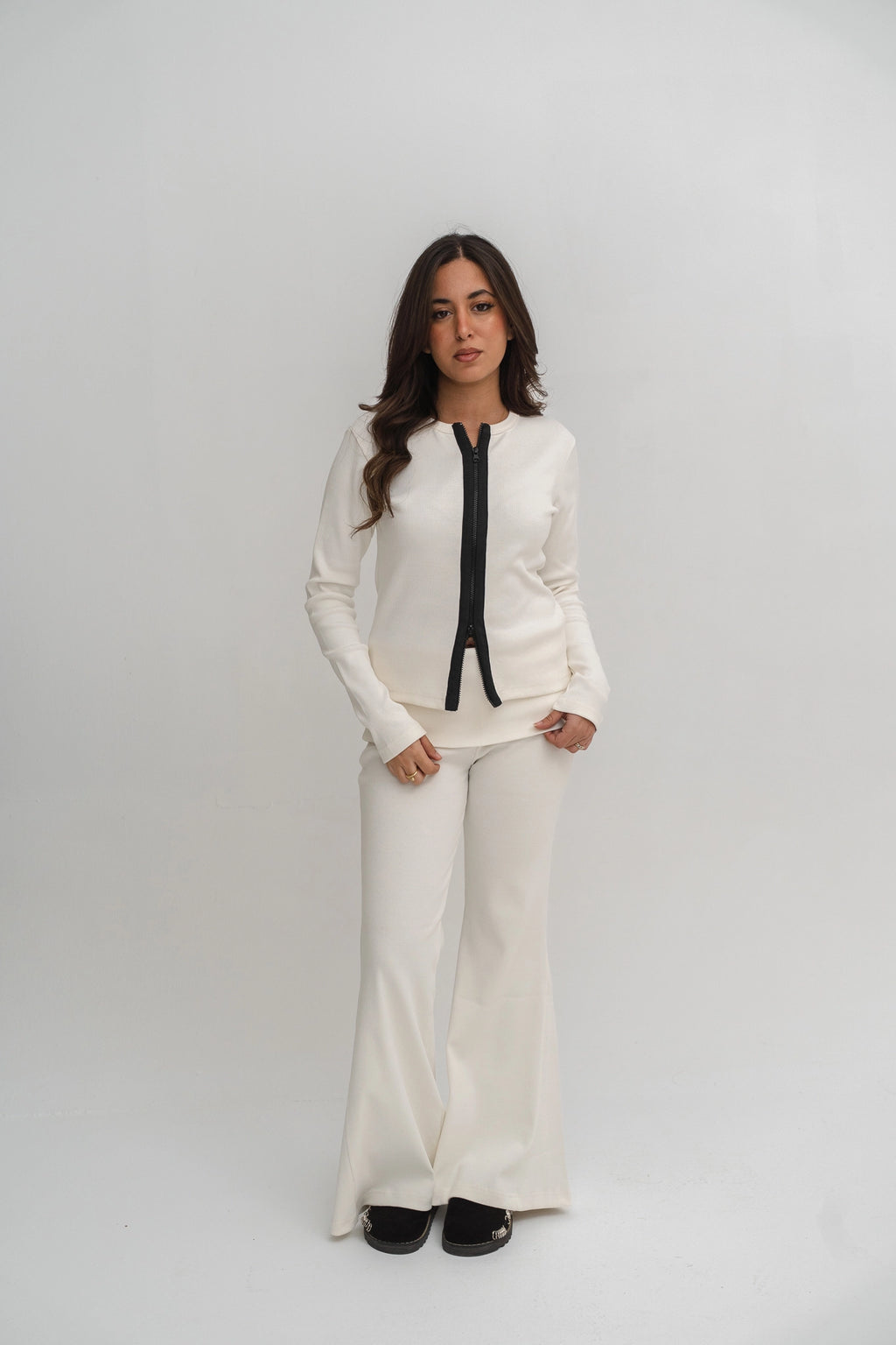 Woman wearing a white outfit with a black tie against a plain background