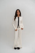 Woman wearing a white outfit with a black tie against a plain background