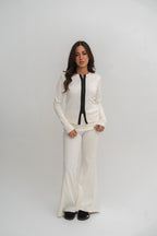 Woman wearing a white outfit with a black tie against a plain background