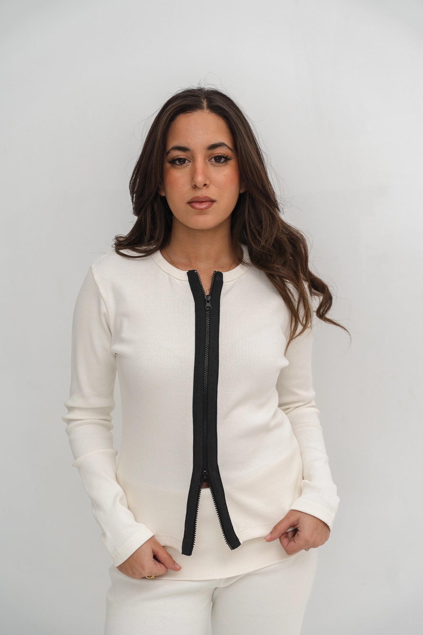 Woman wearing a white long-sleeve top with a black zipper on a plain background