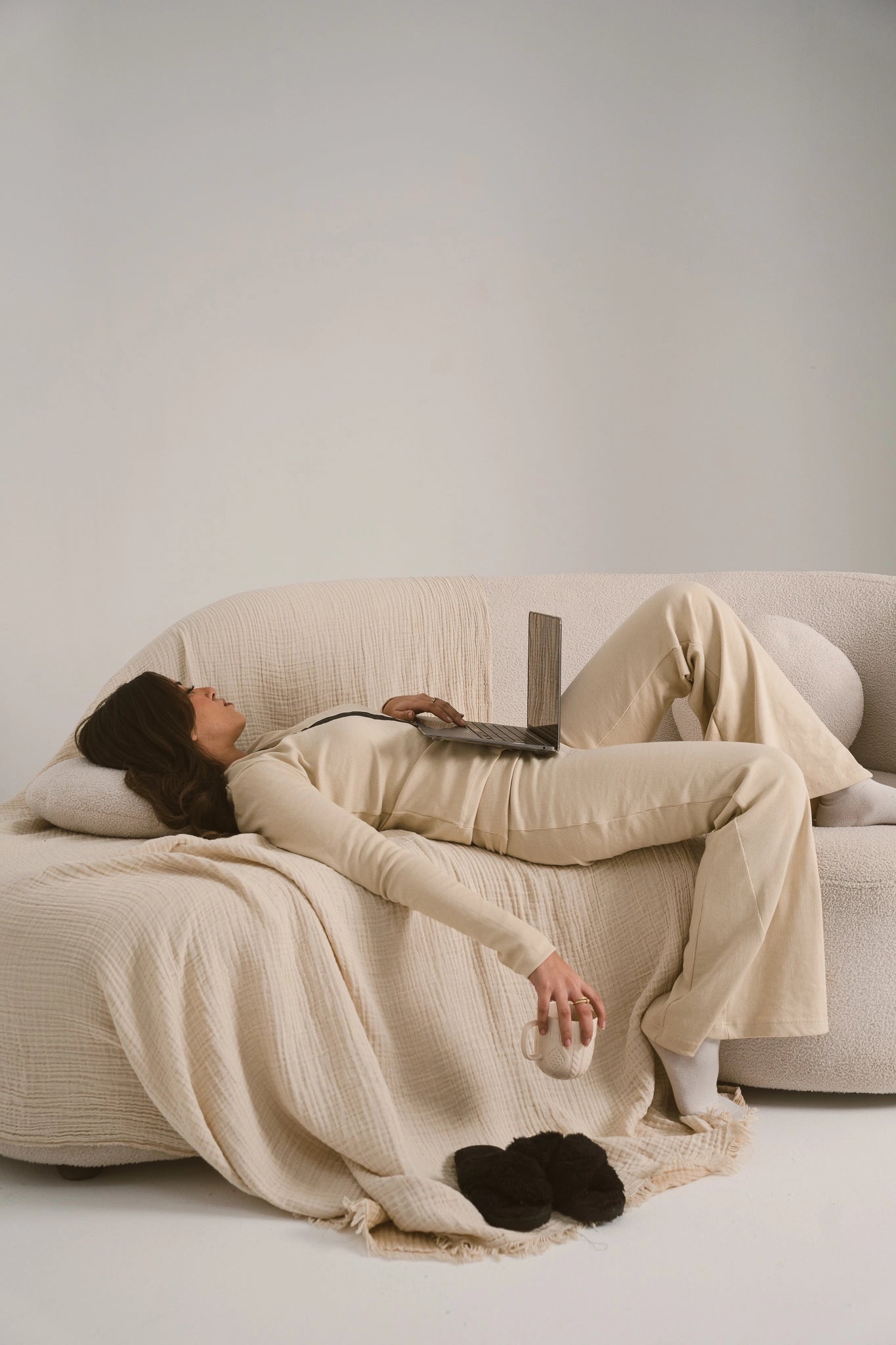 Person lying on a couch with a blanket and laptop in a minimalistic room
